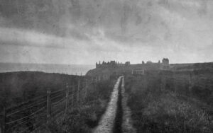 A coastal dirt road near the North Sea, with the ruins of Dunnottar Castle emerging from the ethereal mist.