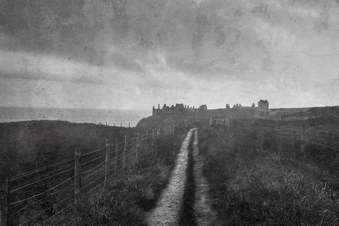 A coastal dirt road near the North Sea, with the ruins of Dunnottar Castle emerging from the ethereal mist.